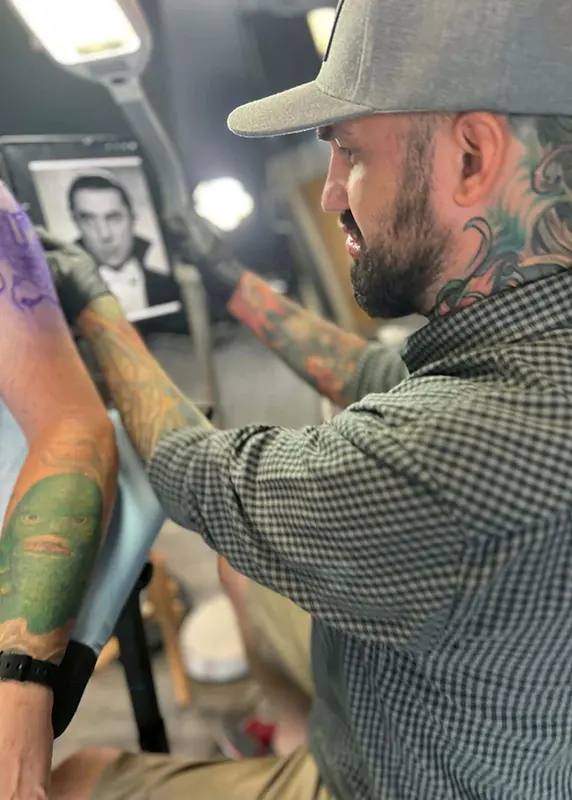 Joshua Hibbard referencing artwork during a tattoo design consultation in his Portland studio.