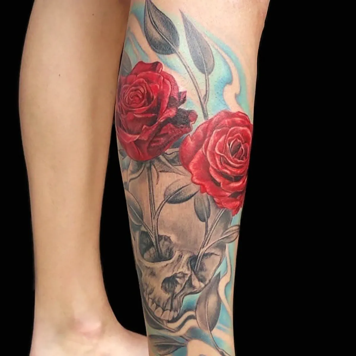 Color tattoo featuring red roses above a shaded skull on the lower leg.